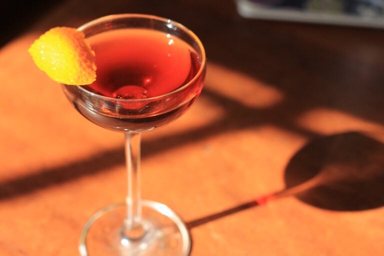 Perfect Manhattan cocktail garnished with an orange zest in a coupe glass.