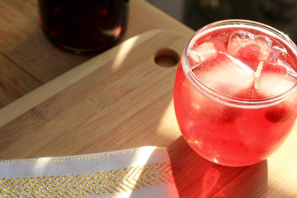 Merry Christmas cocktail in a glass with ice and cherries on a table next to a bottle of Elysium Black Muscat Dessert Wine.