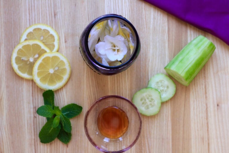 Looking inside a mason jar with edible flowers surrounded by lemons, mint and cucumber.