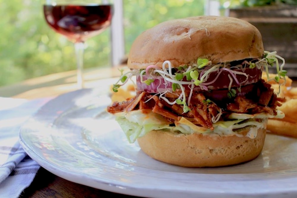 Pulled pork BBQ Jackfruit Vegan Sandwich on a plate with a glass of wine in the background.