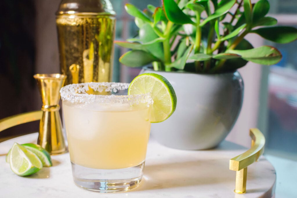Essensia Margarita Cocktail Recipe in glass with lime garnish sitting on a table