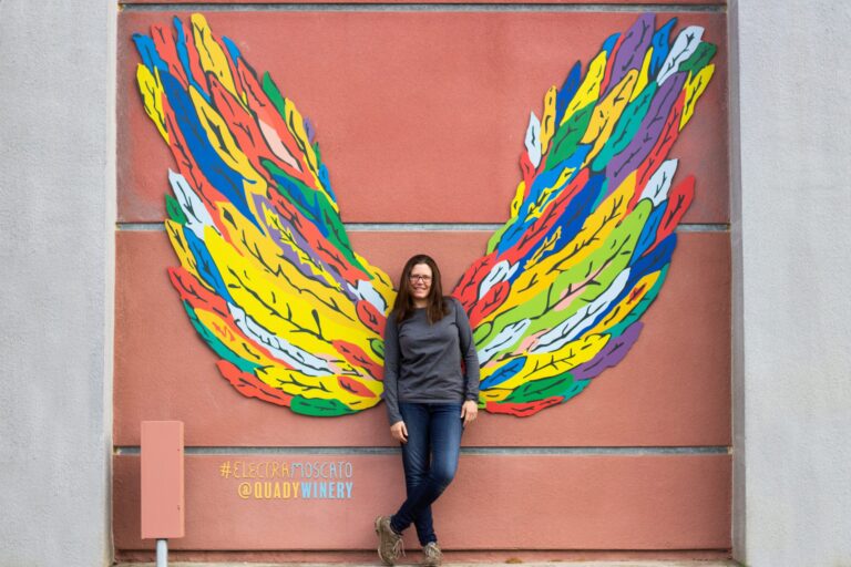 Allie Quady standing infront of Quady Winery's new Electra Moscato wing wall featured at their winery.