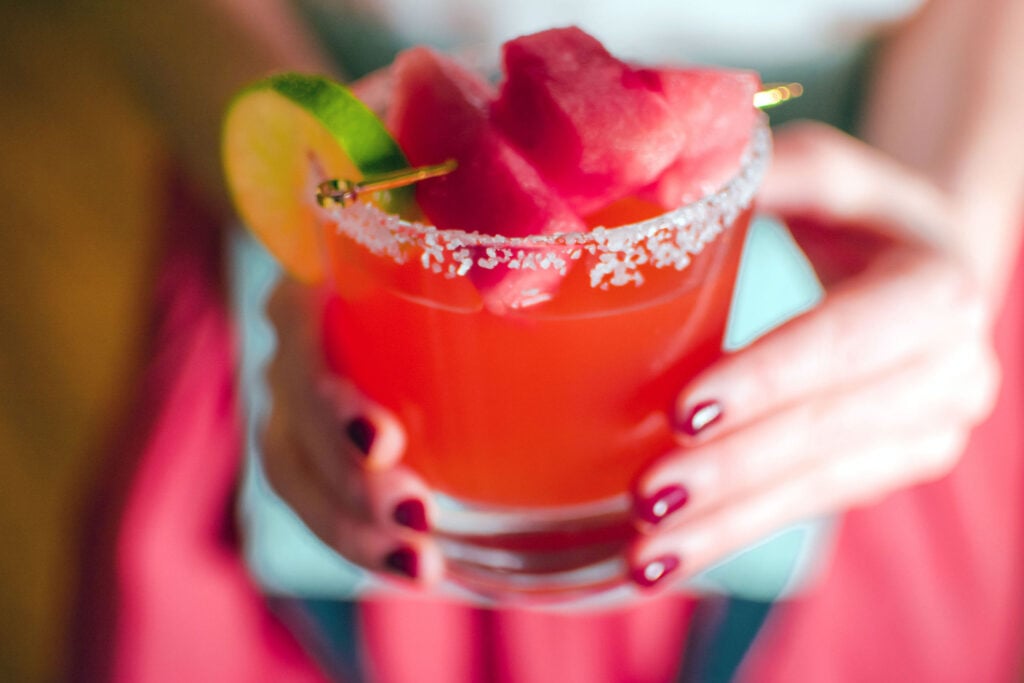 Two hands holding Quady Watermelon Margarita with Red Electra Moscato, Watermelon and tequila in a rocks glass