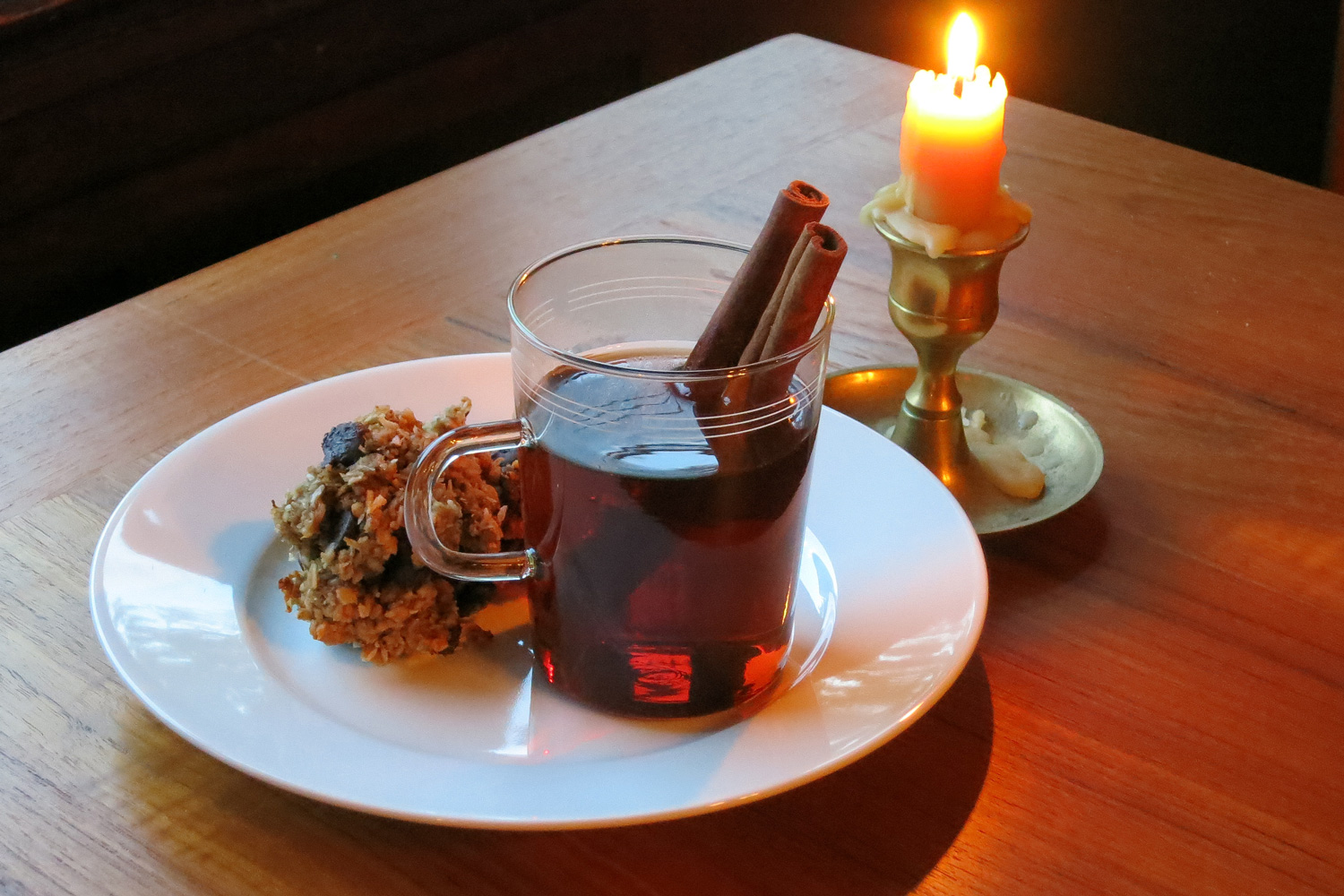 Mug of Mulled Vya winter cocktail with cinnamon sticks, next to a pastry and lit candle.