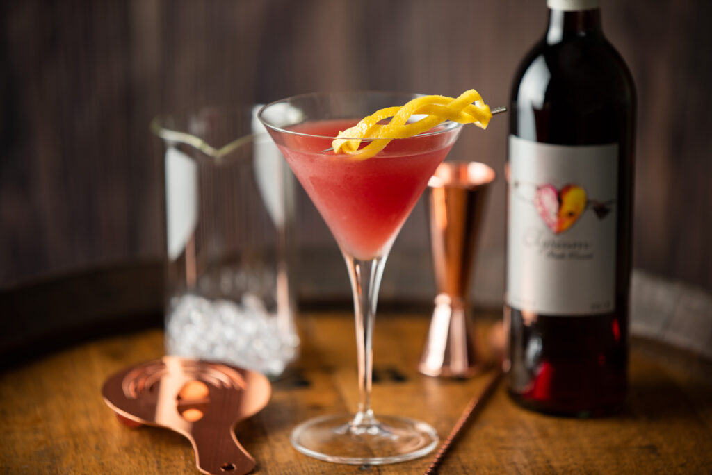 Elysium french martini cocktail in a martini glass next to barware and a bottle of Elysium Black Muscat dessert wine by Quady Winery.