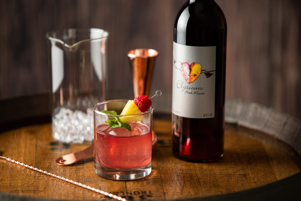 Elysium paloma cocktail in a cocktail glass next to barware and a bottle of Elysium Black Muscat dessert wine by Quady Winery.