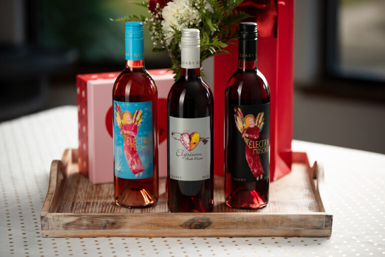 Rose, Elysium, and Red Electra sitting on a table in front of flowers and a box with a heart on it while all standing on a brown tray