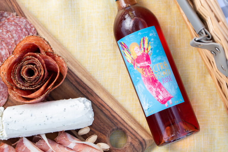 Bottle of Electra Moscato Rosé on a picnic blanket next to a charcuterie board.