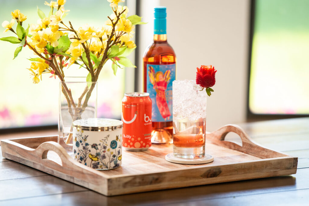 Electra Strawberry Rosé wine cocktail on a table next to a can of strawberry bubly and bottle of Electra Moscato Rosé.