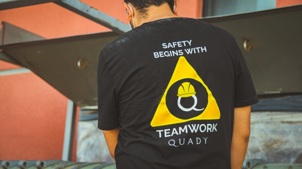 Quady crew member wearing safety shirt standing in front of a machine