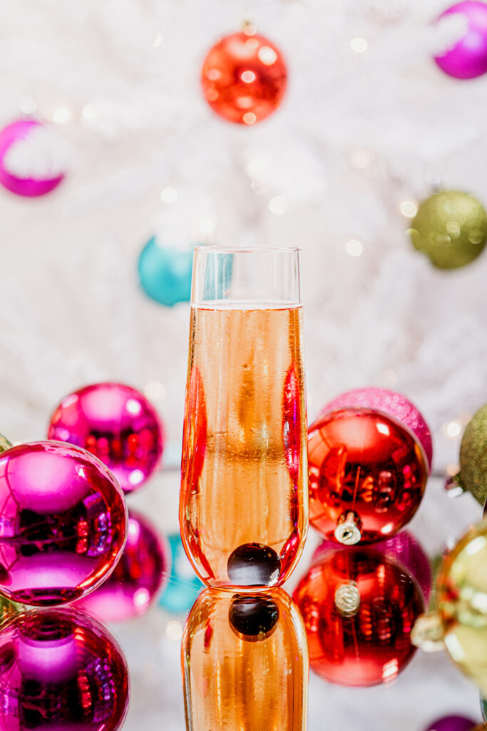 Haute Holiday Sparkling Wine Cocktail with ornaments and a Christmas tree in the background