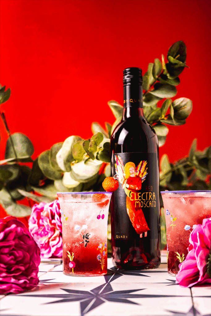Two Raspberry Lemonade Moscato Spritzers with a bottle of Red Electra and flowers and plants
