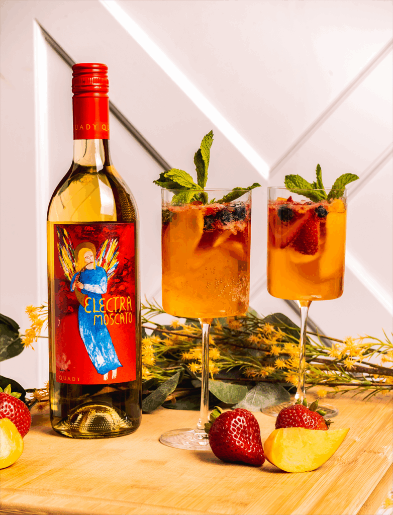Two glasses of Summer Sangria with a bottle of Electra Moscato, peach slices and strawberries